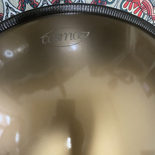 Close-up detail of golden handpan with "Cosmos" logo engraved on the back, showcasing craftsmanship and metallic finish.