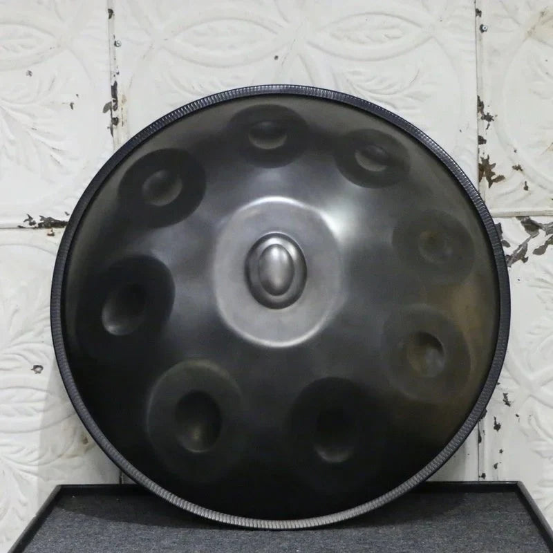 Black handpan drum leaning against a wall, showcasing its sleek design and matte finish.