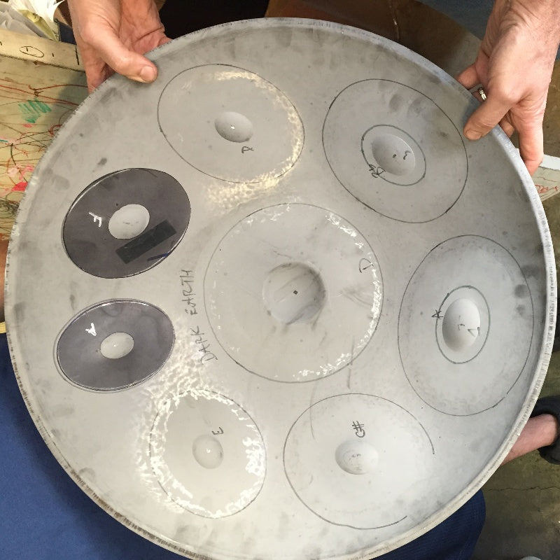 A skilled craftsman tuning a handpan drum, carefully adjusting each note field for perfect pitch and resonance.