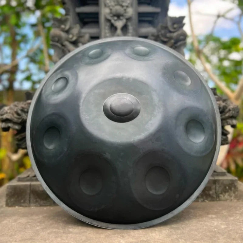 Matte-colored handpan leaning against a garden statue, blending musical art with serene outdoor decor.