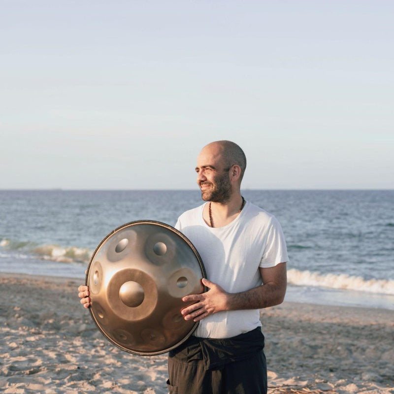 Golden handpan displayed by bald artist on the beach