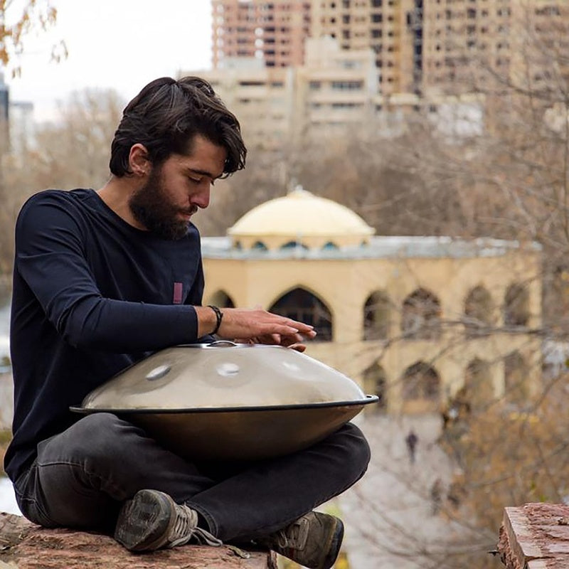 European man playing handpan drum beside an old castle.