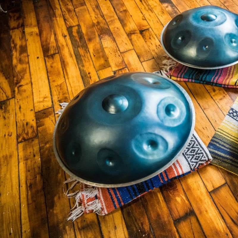 Two handpan drums placed on a wooden floor with a carpet.
