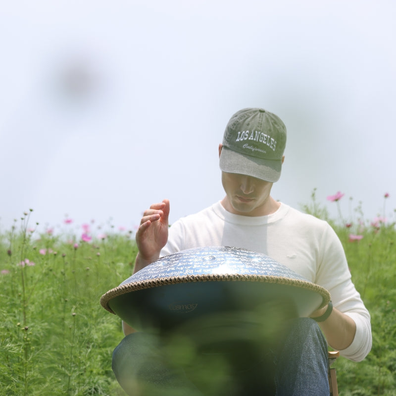 Handpan player in a colorful flower garden using a Cosmoshandpan to create relaxing ambient music.