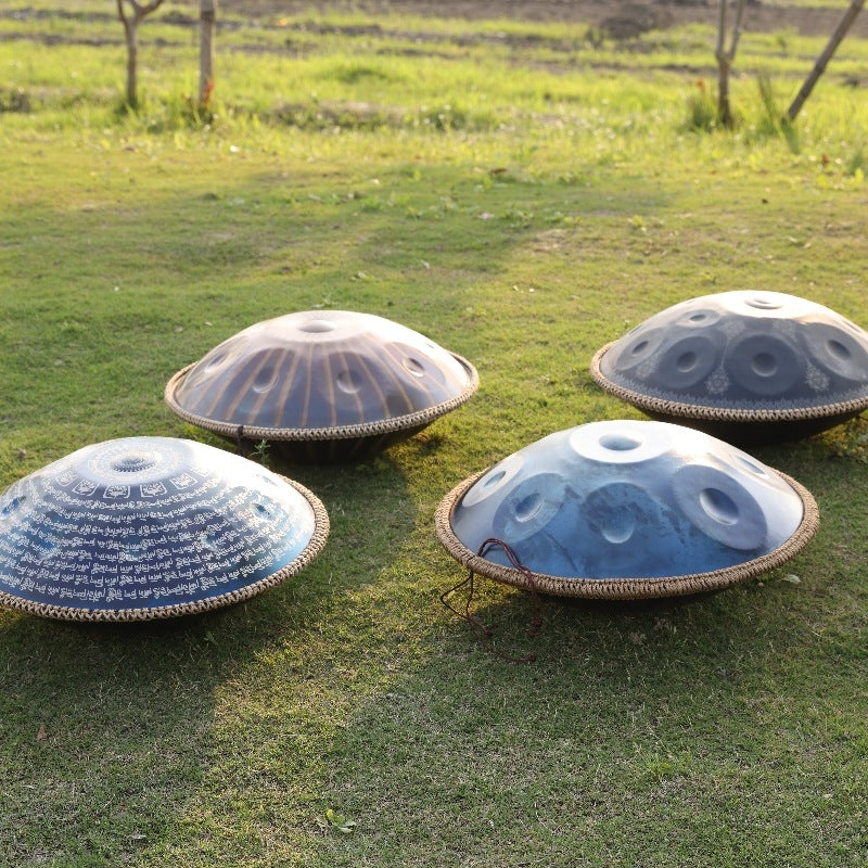 Four decorative handpans with unique designs displayed on green grass under sunlight