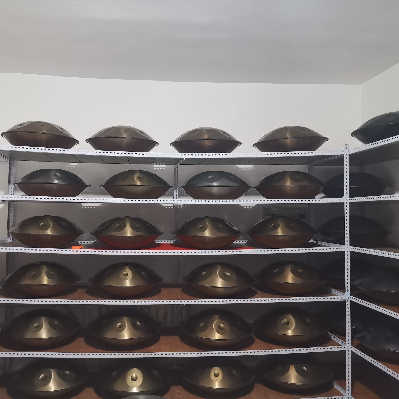 Handpan drums displayed on storage shelves in a tuning workshop, showcasing various colors and sizes of steel melodic percussion instruments