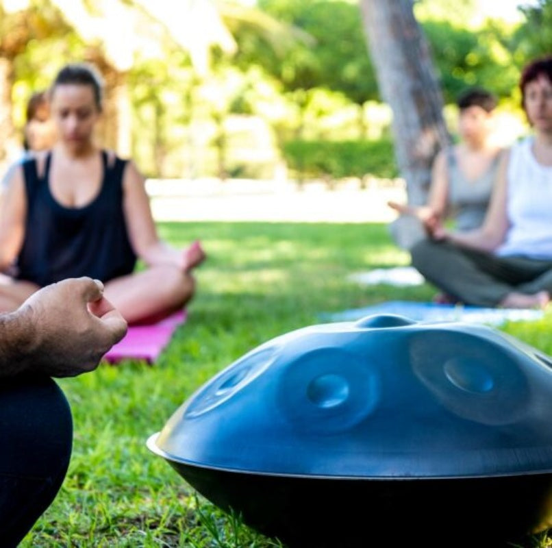 A group of people meditating outdoors while listening to calming handpan music.
