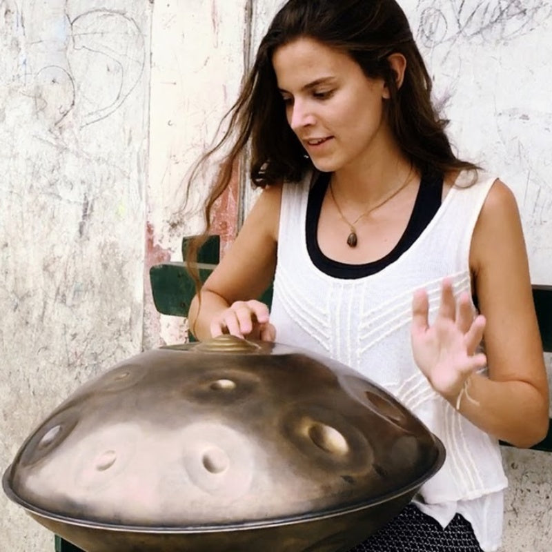 Woman passionately playing handpan drum while sitting on a bench.