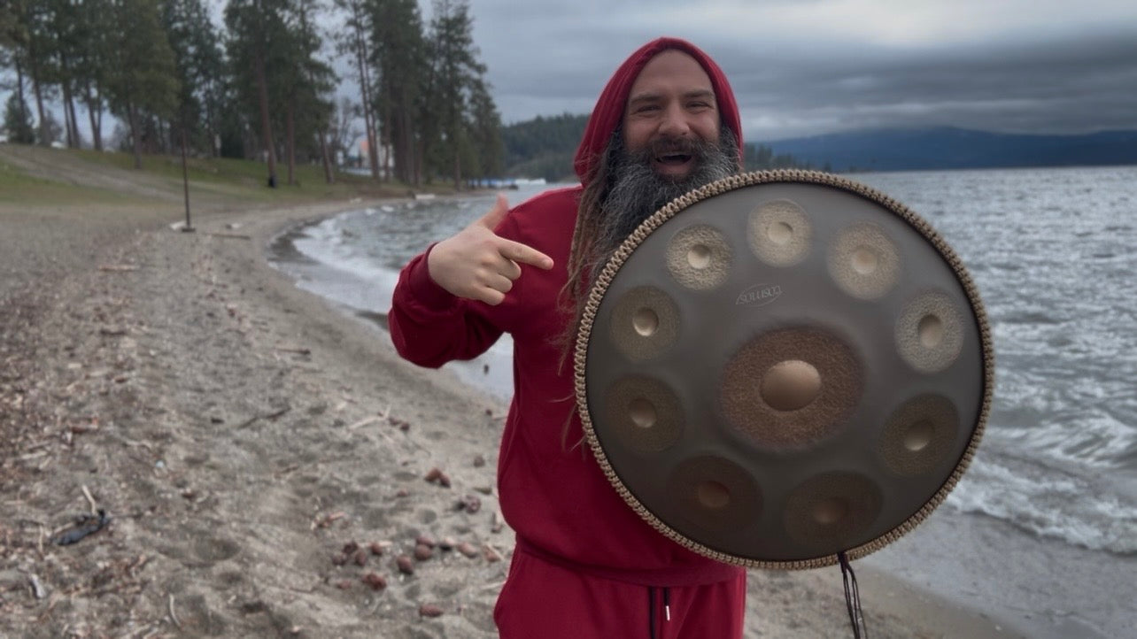 Person in red outfit holding a handpan by a lake